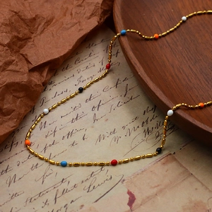 Close-up of golden chain necklace with colorful enamel beads on vintage paper