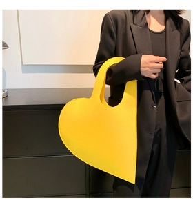 Detail of a bright yellow heart-shaped felt handbag held by a model in a black suit