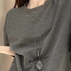 Detail of silver grid square pendant necklace with black ribbon bow on a grey tshirt