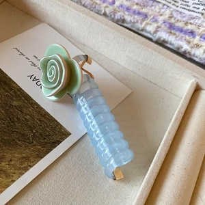 Détail d'une pince à cheveux spirale avec rose verte et texture acrylique bleue