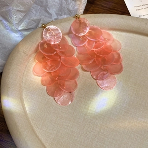 Detail of pink shell petal drop earrings layered with gold studs on a beige display plate