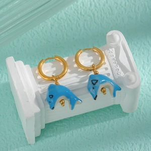 Détail de boucles d'oreilles créoles dorées avec dauphins en céramique bleue sur socle