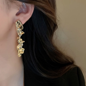 Close-up of model wearing gold irregular fluid design long earrings with metallic finish