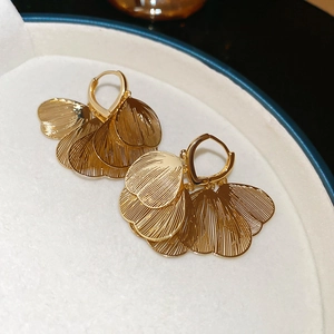 Macro shot of gold shell petal earrings on a white jewelry plate with warm lighting