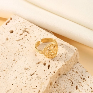 Detailed shot of a gold-plated snake-pattern hollow ring on beige stone and satin