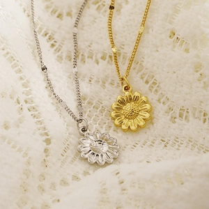 Eleganti collane con ciondolo a girasole in oro e argento su sfondo di pizzo bianco
