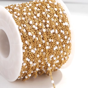 Macro shot of gold plated stainless steel cable chain with white enamel beads on a reel