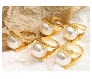 Detail of five gold geometric rings with large white pearls on natural textured paper