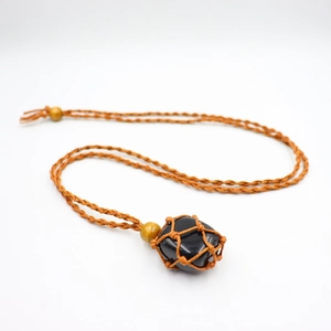 Macro detail of natural black stone pendant with handcrafted orange woven mesh and wooden beads