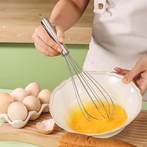 Manual stainless steel egg whisk with ergonomic round handle used in a professional kitchen