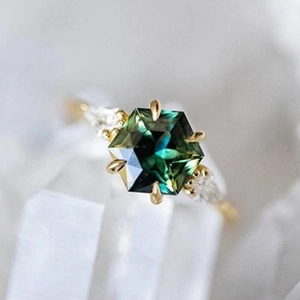 Elegant gold ring with hexagon green gemstone and side diamonds on crystal block