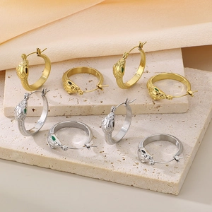 Detailed view of gold and silver snake head earrings with green eyes on beige stone