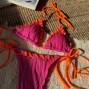 Detail of pink and orange ribbed bikini with crisscross ties and silver metal eyelets