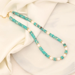 Fashionable turquoise and pearl beaded necklace with gold accents on white satin