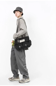 Close-up of black messenger bag with multi-pockets and a cute green dinosaur charm