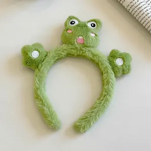 Gros plan sur le serre-tête grenouille en peluche verte avec yeux brodés et fleurs 3D