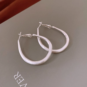 Macro shot of silver oval hoop earrings with brushed metal texture and matte finish