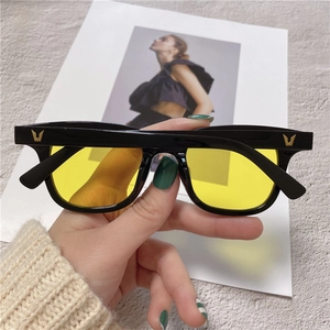 Close-up of square black sunglasses with yellow lenses and golden V-shaped metal logo