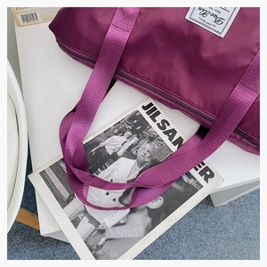 Close-up of purple waterproof nylon travel bag with branded patch on a minimalist setup