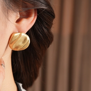 Macro shot of gold geometric earrings with brushed wavy texture worn by a model