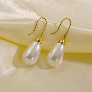 Close-up of elegant gold teardrop pearl earrings on a soft beige silk background
