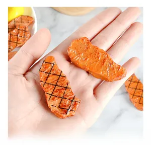 Macro shot of a mini realistic grilled steak PVC model held between fingers