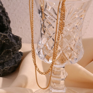 Detail of 18K gold double layer necklace hanging on crystal glass with snake chain texture