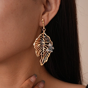 Close-up of a large golden hollow leaf earring with a small silver flower detail