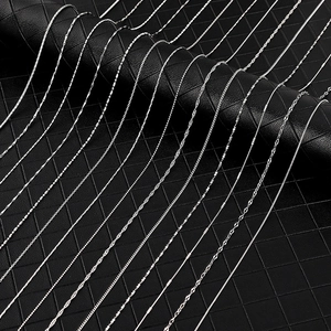 Detail of silver box, snake, and water wave chains on black quilted texture