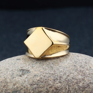 Dettaglio di un anello geometrico dorato in acciaio inossidabile su sfondo di pietra naturale