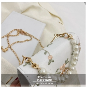 Detail of white embroidered small square bag with pearl handle and golden chain strap