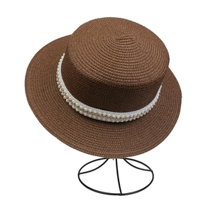 Detail of dark brown straw hat featuring white pearls and a gold chain decorative band
