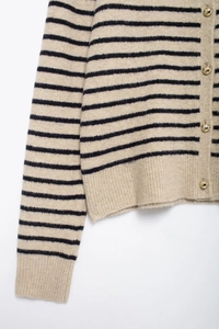 Detail of beige striped knit cardigan featuring golden buttons and ribbed cuffs