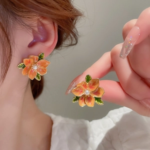 Detailed close-up of orange enamel flower earrings with green leaf and white pearl accent