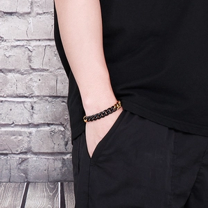 Close-up of a men's dual-tone black and gold Cuban link bracelet on a model's wrist