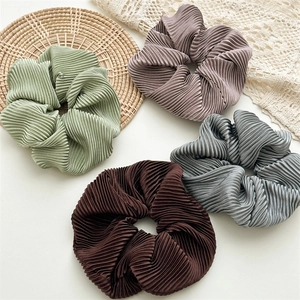 Set of four oversized silky pleated scrunchies in muted tones on a decorative lace background