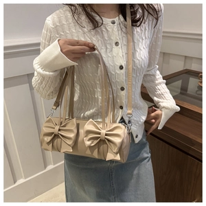 Model holding a beige cylinder bag with oversized bows and silver hardware