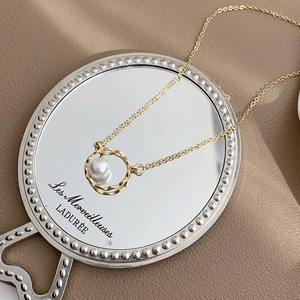 Close-up of a geometric gold pearl necklace elegantly resting on a vintage mirror surface