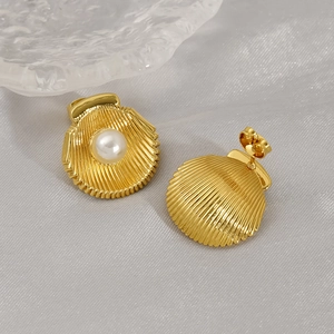 Élégantes boucles d'oreilles coquillage dorées avec perle sur fond doux texturé