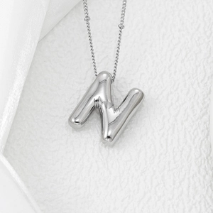 Polished silver balloon letter N pendant necklace on white satin and textured surface
