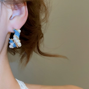 Close-up of C-shaped pearl denim twist earrings worn by model with gold wire detail