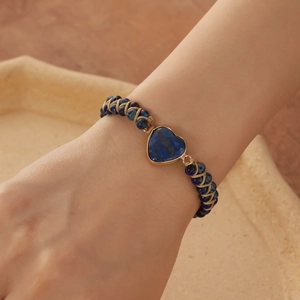Detailed view of hand-woven bracelet with heart-shaped blue emperor stone on female wrist