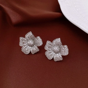 Macro shot of silver flower earrings with clear pavé zircons on dark silk fabric