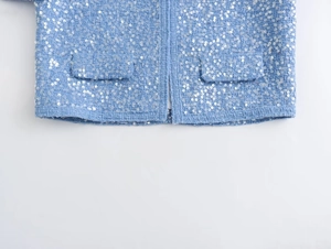 Close-up of light blue tweed jacket with sequin texture and double pocket stitching detail