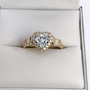 Anello con gemma a cuore esagerata, diamanti halo e finitura dorata su scatola bianca