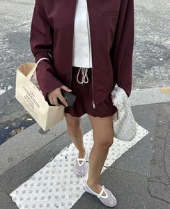 Detail of burgundy zipper jacket and drawstring shorts set with woven handbag