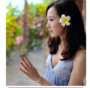 Close-up of a white plumeria flower hair clip worn by a woman in a tropical setting
