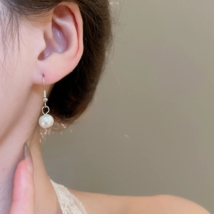 Detail of elegant silver hook earring with a single white pearl worn by a model