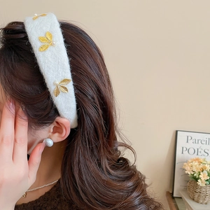Close-up of elegant cream velvet headband featuring golden metal leaves and pearls