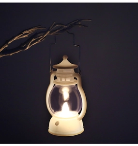 White vintage mini LED lantern hanging on a branch with warm yellow glow effect
